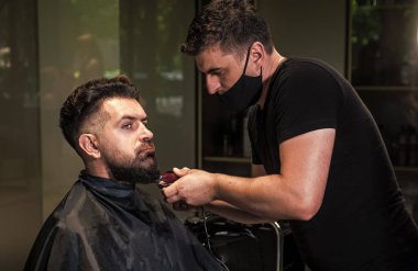 Sihirli bakış. Profesyonel berber ustası olan acımasız adam elektrikli tıraş makinesi kullanıyor. Hipster. Erkek berber bakımı. Kuaför salonundaki sakallı adam. Güzellik ve moda. saç ve sakal şekillendirme