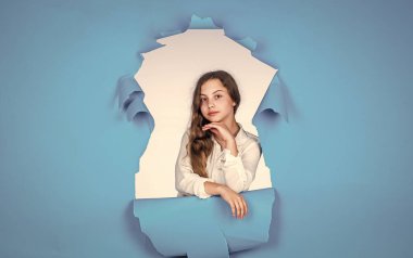 Hırslı ve güzel. Uzun kıvırcık saçlı güzel bir genç kız. Çocuk modası. Doğal dişi güzellik. Mutlu çocukluk. Mavi arka planda sevimli bir çocuk. Kuaför salonu. şık görünüş