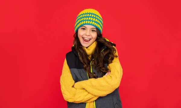 Χειμερινή μόδα. συναισθηματικό χαρούμενο παιδί με σγουρά μαλλιά στο καπέλο. έφηβος κορίτσι σε κόκκινο φόντο. — Φωτογραφία Αρχείου