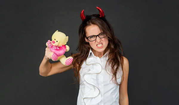 Angry girl with red devil horns make scary face holding Valentines bear dark background, Halloween — Stockfoto