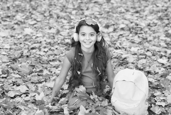 Dinlenme zamanı. Online eğitim kavramı. Çocuk sonbahar yapraklarında oturur. Okul çantalı kulaklıklı kız. Çocuk sonbahar parkında müzik dinler. Sonbahar çalışma zamanıdır. Okula geri dön. — Stok fotoğraf