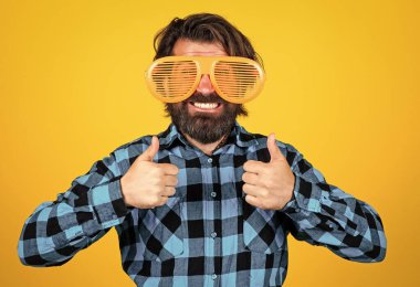 Komik gözlüklü sakallı adam. Vahşi adam kareli gömlek giyiyor. Bıyıklı erkek eğleniyor. Yakışıklı hippi partisi müdavimi. Mutlu olgun bir adam baş parmağını gösteriyor.