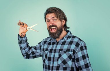 Berber dükkanı konsepti. Kareli gömlekli sakallı adam saç kesiyor. Sıradan bir adam berber aletini kullanır. Uzun saçlı ve bıyıklı mutlu hippi makası tutuyor. Erkek güzelliği ve moda