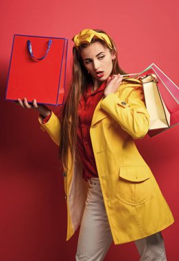 Kırmızı arka planda alışveriş torbaları tutan heyecanlı güzel bir kızın portresi. Alışverişten hoşlanan kadın. Alışveriş torbaları taşıyor. Kadın alışverişçi. Elinde hediye tutan neşeli bir kadın. Mükemmel gün.