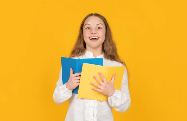 Happy teen girl hold school workbook on yellow background, school — стоковое фото