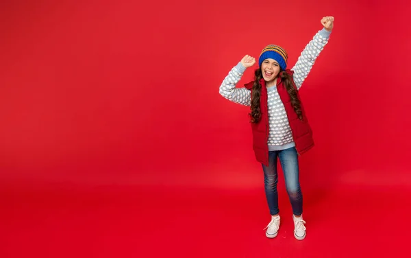 Criança feliz no chapéu de inverno tricotado e colete abaixo no fundo vermelho, espaço de cópia, felicidade — Fotografia de Stock