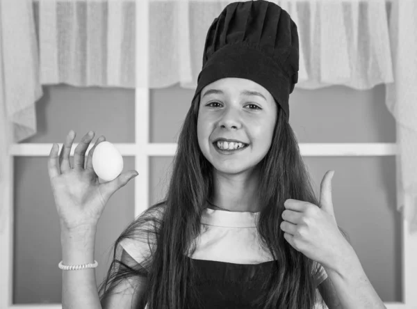 Lapsi valmistaa terveellistä ruokaa kotona ja yllään kokki yhtenäinen. siivous ja kodinhoito. lapsuuden kehitys. pieni tyttö leipoo keittiössä. Keittiömestari laittaa munia. Huikeita tilaisuuksia — kuvapankkivalokuva