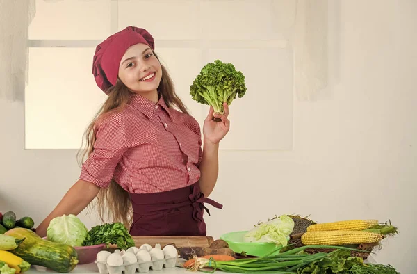 Endast hälsosam ekologisk mat. Full av vitaminer. Ungen bär kockuniform och hatt. Tonårstjej som lagar mat. Färska råa grönsaker. Dags att äta. Grön sallad. Glad barnmat i köket — Stockfoto