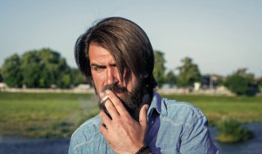 Bıyıklı vahşi sakallı hippi şık bir saç kesimi ve açık havada sigara içen sıradan bir gömlek giyiyor, rahatlıyor.