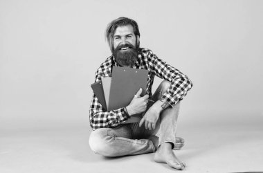 Vahşi sakallı bir adam kareli gömlek giyer. Dolgun sakallı ve bıyıklı. Dosyasında belgeler, evrak işleri vardır.