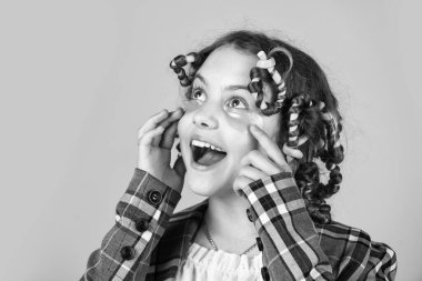 Göz bantlı mutlu çocuk. Kuaför salonu. Sarı arka planda saç tokası ve saç tokası olan bir kız. Saçlarının etrafında kıvırcık kızlar. Güzel bir saç stili yap. Harika bir saç stili.