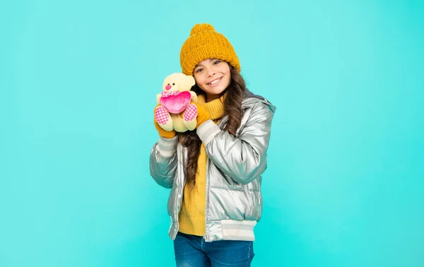 Kışın giyinmiş neşeli genç kız mavi arka planda oyuncak tutuyor, sevgililer gününde. — Stok fotoğraf