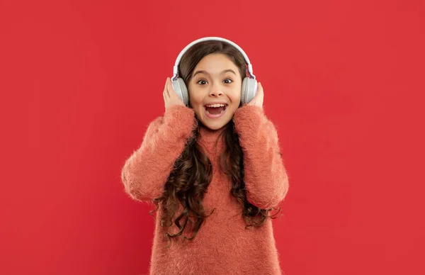 Amazed teen girl in sweater in headphones for listening music, childhood — Zdjęcie stockowe