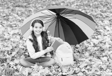 Neşeli genç çocuk sonbahar ormanlarında ya da parkta kulaklıkla müzik dinlerken renkli şemsiyeler altında okul çantasından kitap alıyor, e-öğreniyor.