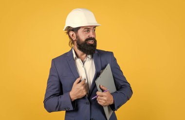 Mimari ve bina. Erkek müteahhit koruma için resmi takım elbise ve kask giyiyor. İnşaat projesinde çalışıyorum. Sakallı gülümseyen adam sert şapka takıyor. mühendislik kavramı