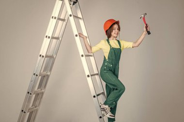 Kız çocuğu üniforma ve kask giyer atölyede çalışırken merdivende çekiçle, kariyerle