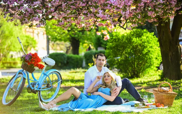Expressing feelings. enjoying nature together. having picnic in city park. man and woman relax with food basket. Romantic traveler couple under sakura blossom tree. couple in love on green grass — Stock Photo, Image