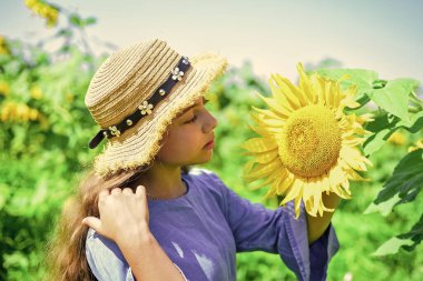 Neşeli bir hafta sonu. Çiçekli güzel çocuk. Yaz doğasının güzelliği. Ayçiçeği tarlasında küçük bir kız. Ayçiçeğinin sarı çiçeği. Mutlu çocukluk. Güzel kız tarlada hasır şapka takıyor.