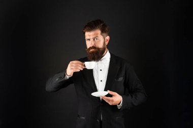 Smokinli papyonlu, elinde kahve fincanı olan adam. Formalite içindeki beyefendi siyah arka planda kahve içiyor.