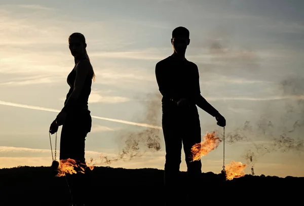 Couple of man and woman in dark silhouettes perform burning poi dance during fire performance on idyllic evening sky outdoors, smoke — Stock Photo, Image