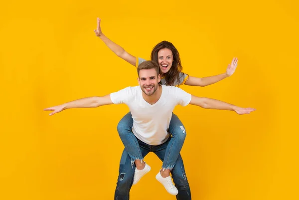 Happy couple in love of girl and man pretend flying doing piggyback ride yellow background, playful — стоковое фото