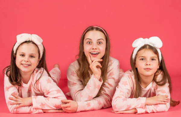 Portrait of girls with surprised faces lying in pajamas pink background — стоковое фото