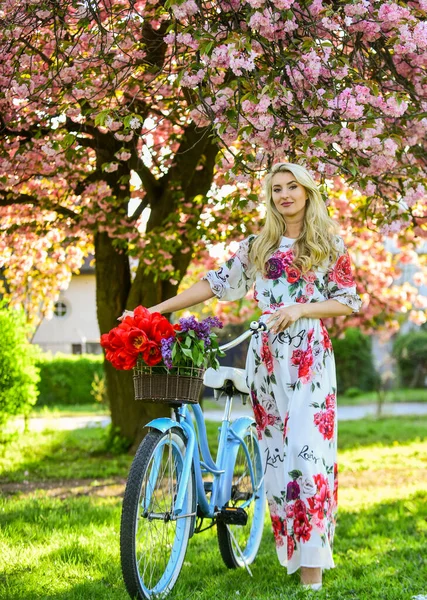 Spring beautiful woman in dress. girl with vintage bike. blooming sakura tree. summer fashion and beauty. lady walk in park. pink cherry tree blossom. girl carry flowers in retro bicycle — Stock Fotó