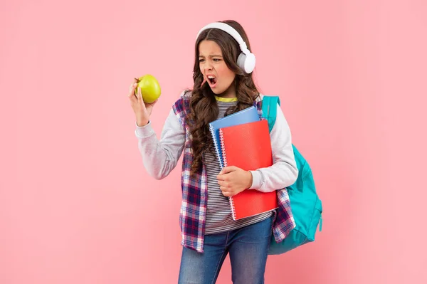 가방 과 헤드폰을 끼고 사과와 점심을 먹고 있는 10 대 소녀가 놀란 모습입니다.. — 스톡 사진