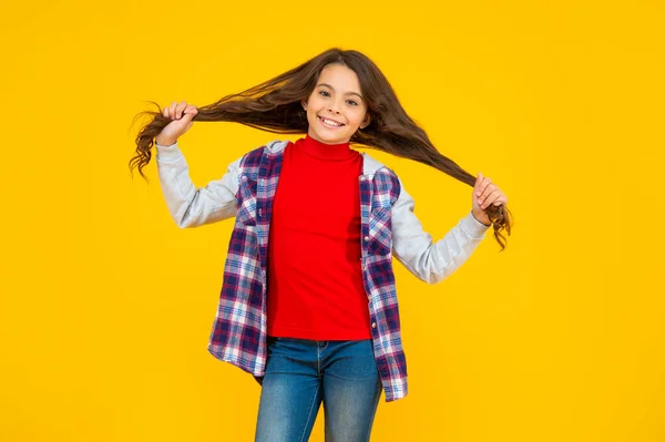 Щаслива дитина випадкового стилю тримає довге волосся на жовтому фоні, волосся — стокове фото