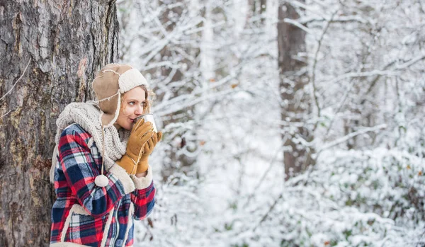 Zimowy napój. Dziewczyna lubi opady śniegu. Kobieta w rękawiczkach i kapeluszu pijąca herbatę w śnieżnym lesie. Na dworze w mroźny dzień. podróże i wędrówki. Dziewczyna turysta pić filiżankę gorącej herbaty. Rozgrzej się. — Zdjęcie stockowe
