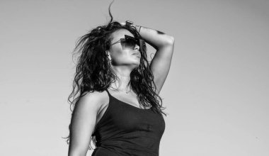 Seksi esmer kadın uzun kıvırcık saçlı şık güneş gözlüğü takıyor ve yaz havasının, modanın ve güzelliğin tadını çıkarıyor.