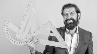 Kostümlü olgun sakallı öğretmen. Okulda tahtası ve ölçüsüyle otur.