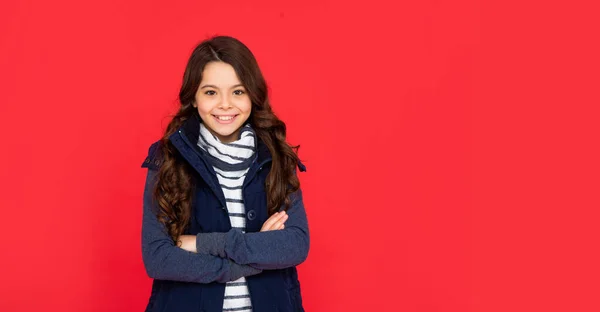 Criança alegre com cabelo encaracolado no colete puffer. menina adolescente no fundo vermelho. — Fotografia de Stock