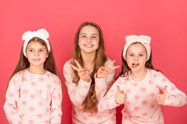 A dar polegares duplos e sinais em V. Meninas felizes em homewear fundo rosa. Crianças roupa de casa — Fotografia de Stock
