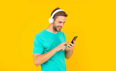 Cep telefonundan mesaj atan, kulaklıkla dijital müzik dinleyen mutlu genç adam.