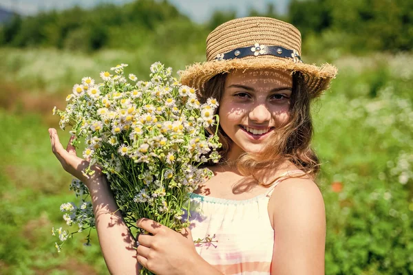 Happy kid with healthy baby skin smile with romomile flowers natural floral spa and beauty care in sun hat on sunny summer landscape, skincare — стоковое фото