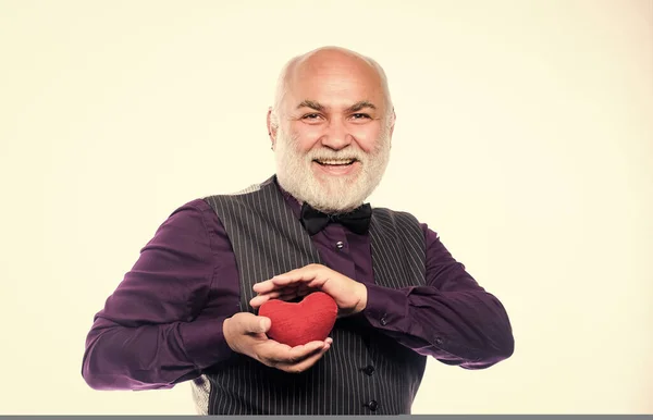 Gezondheidszorg. Hartinfarct voorkomen. Senior kale man met een baard die een rood speelgoedhart in handen houdt. Volwassen man met een hart van Valentijn. Hartproblemen en gezondheidszorg. Hartslagdiagnostiek en behandeling — Stockfoto