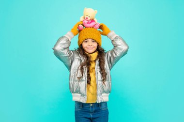 Şapkalı ve kabarık ceketli neşeli çocuk mavi arka planda oyuncak, hediye