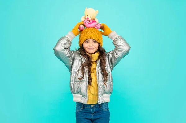 Criança alegre em chapéu e jaqueta de puffer com brinquedo em fundo azul, presente — Fotografia de Stock