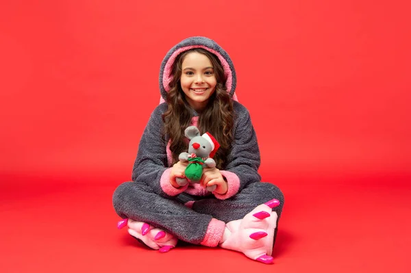 Gelukkig kind in gezellige slaapkledij zitten met kerst speelgoed op rode achtergrond, nieuwjaar — Stockfoto