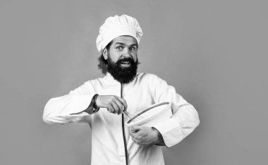 Sevgiyle yapılmış. Sakallı ve bıyıklı yakışıklı adam yemek pişiriyor. Profesyonel restoran aşçısı pişirme. Becerikli fırıncı yemek pişirmek için mutfak aletleri kullanır. Şapkalı erkek şef sağlıklı bir yemek hazırla.