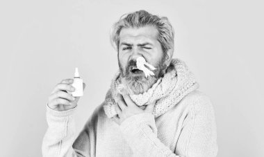 Eşarplı adam burun spreyi ve doku tutuyor. Soğuk algınlığı ilaçları. Burnu akıyor ve soğuk algınlığının diğer belirtileri. Buruna damlatıyor. Çin 'den gelen koronavirüs. Hapşırmamaya çalışıyorum. Burun nezlesi ya da alerji.