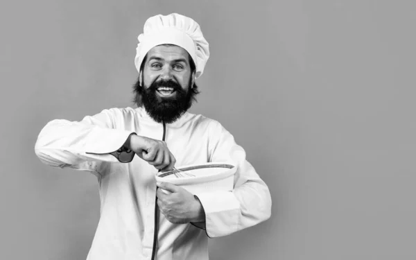 Alegre chef masculino em chapéu com barba e bigode no fundo laranja batendo refeição com batedor, cozinha, espaço de cópia — Fotografia de Stock