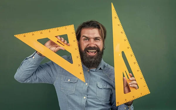 測定と大きさ。三角形の道具を持つ幸せな成熟した教師。髭の男は支配者と教室で働いてる。幾何学試験の準備を。数学の講師をしています。学校に戻って。正式な教育は — ストック写真