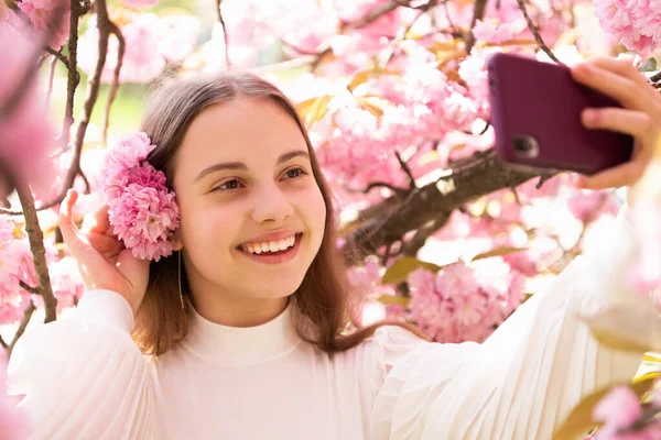 Ritratto di bambina felice che prende selfie con smartphone al ciliegio sakura fiorito in primavera — Foto Stock