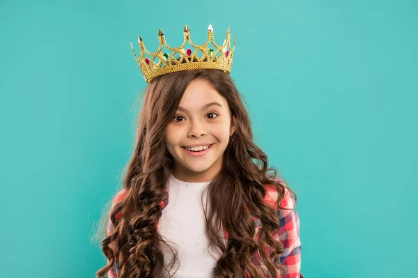 Glimlachend kind met krullend haar in koningin kroon op blauwe achtergrond, zelfvoldaan — Stockfoto