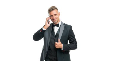 Smokinli neşeli beyefendi beyaz arka planda izole bir şekilde telefonda konuşuyor. başparmak yukarı