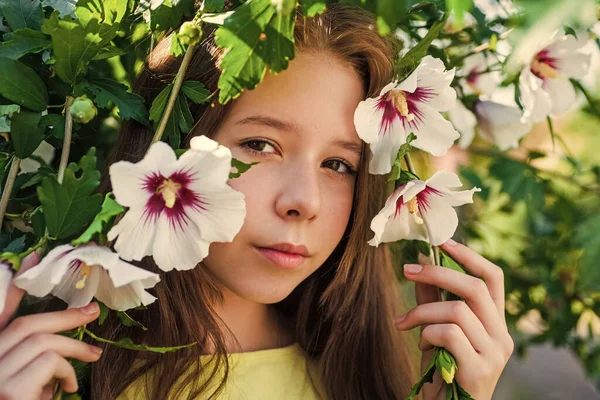 幸せな子供時代。屋外の木の開花時に明るい子供。休暇の時間だ。夏のファッションと美しさ。ハイビスカスの茂みの花を持つ美しい10代の女の子。子供の春ファッションスタイル — ストック写真