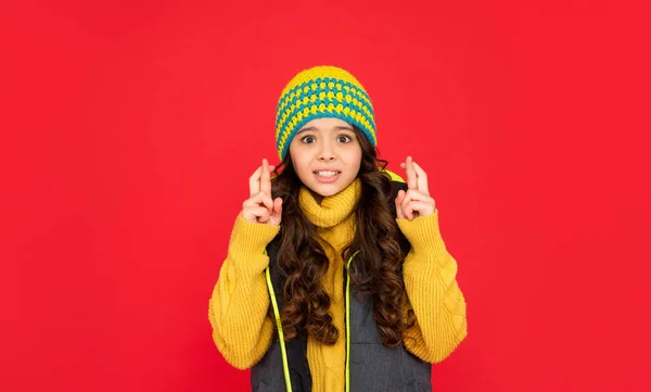 Σταύρωσε τα δάχτυλα. Μπερδεμένο παιδί με σγουρά μαλλιά στο καπέλο. έφηβος κορίτσι σε κόκκινο φόντο. — Φωτογραφία Αρχείου