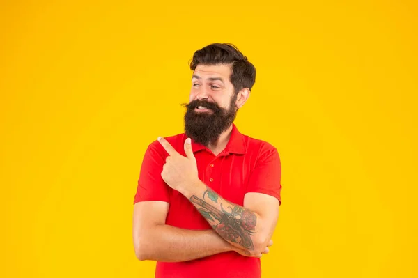 Glad hipster hane med skägg pekar finger på gul bakgrund, mens skönhet — Stockfoto